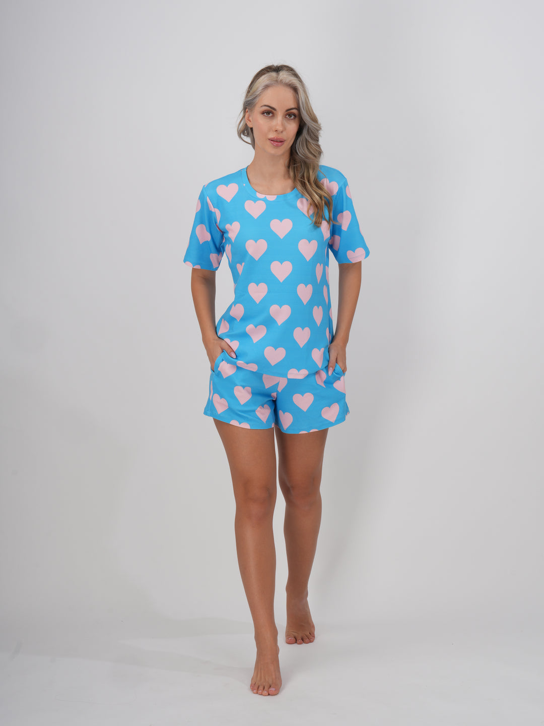 A female model wearing a blue short set with round neckline and heart patterns on the sleeves and shorts - Dreamy Hearts Short Set.