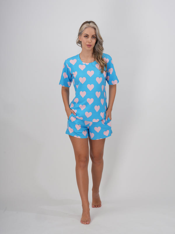A female model wearing a blue short set with round neckline and heart patterns on the sleeves and shorts - Dreamy Hearts Short Set.