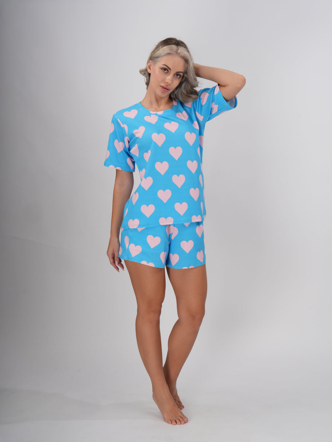 A female model wearing a blue short set with round neckline and heart patterns on the sleeves and shorts - Dreamy Hearts Short Set.