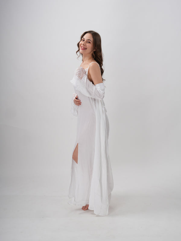 A woman standing wearing a white, full-length robe with lace detailing on the sleeves and neckline - Ethereal Grace Robe Set