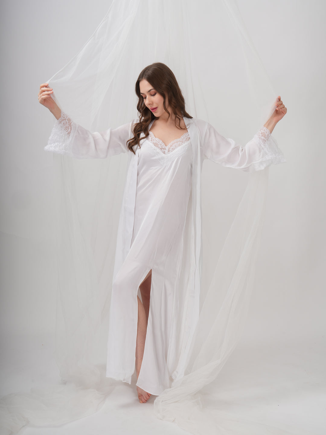 A woman standing wearing a white, full-length robe with lace detailing on the sleeves and neckline - Ethereal Grace Robe Set