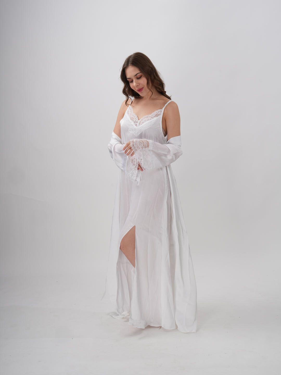 A woman standing wearing a white, full-length robe with lace detailing on the sleeves and neckline - Ethereal Grace Robe Set