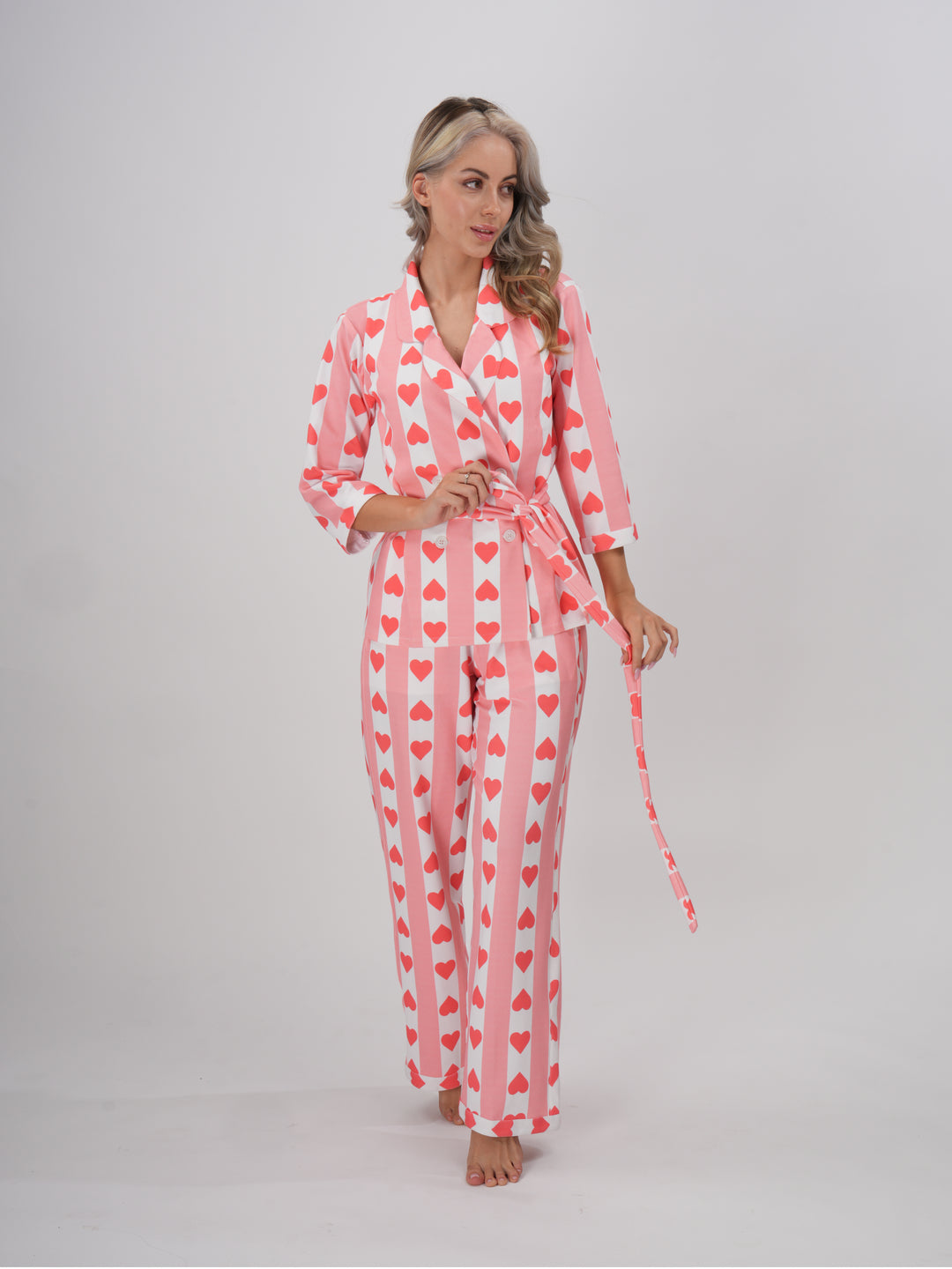 A model wearing a pink hearts pajama set with a collar and full sleeves. The set includes a detachable belt -Hearts & Hush PJ Set
