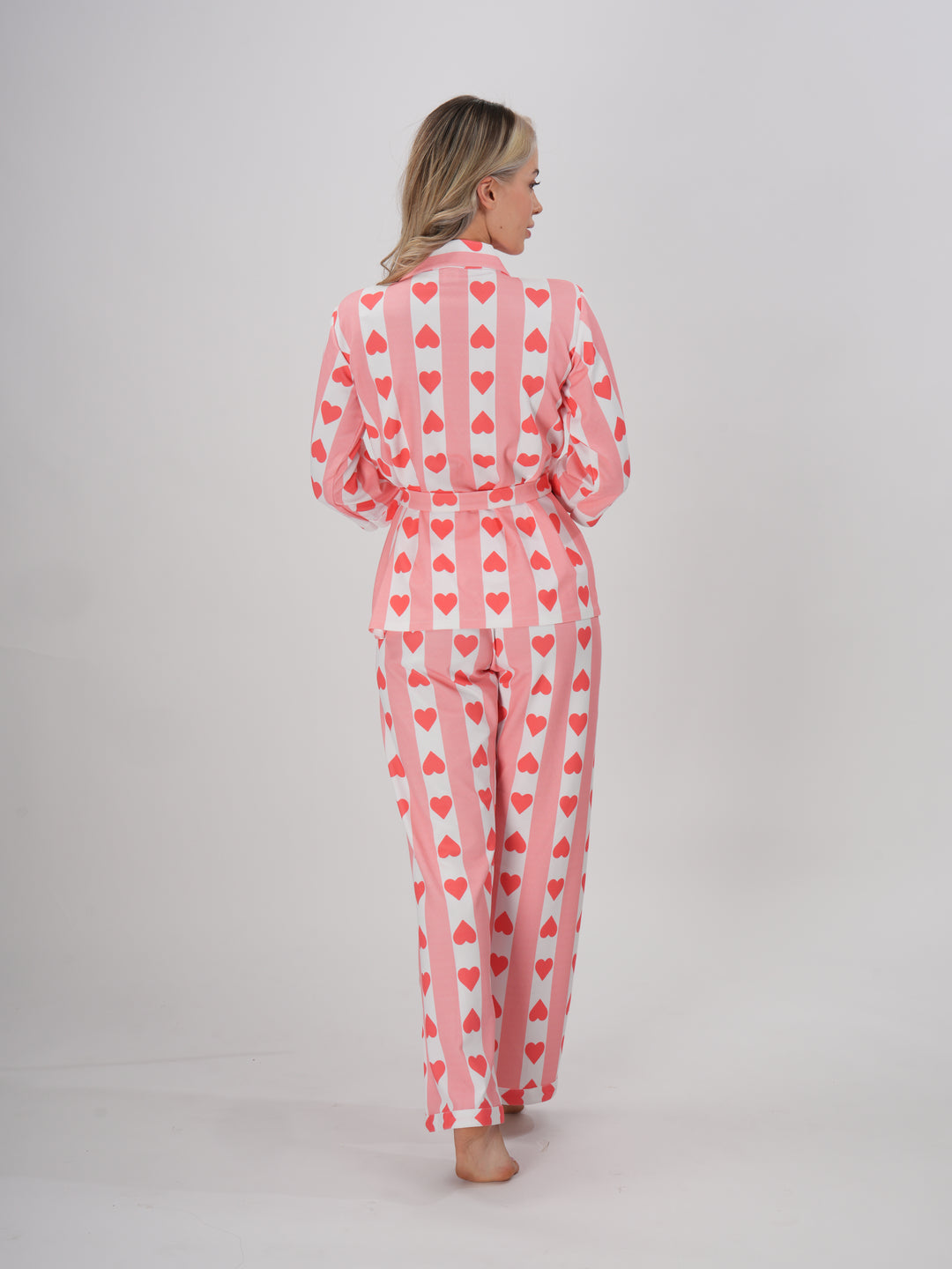 A model wearing a pink hearts pajama set with a collar and full sleeves. The set includes a detachable belt.