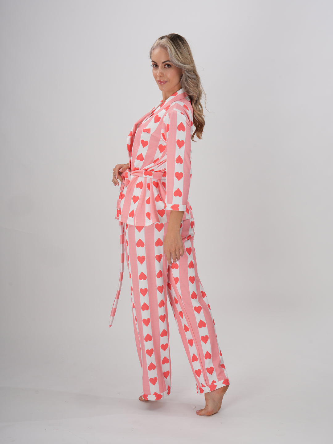A model wearing a pink hearts pajama set with a collar and full sleeves. The set includes a detachable belt.