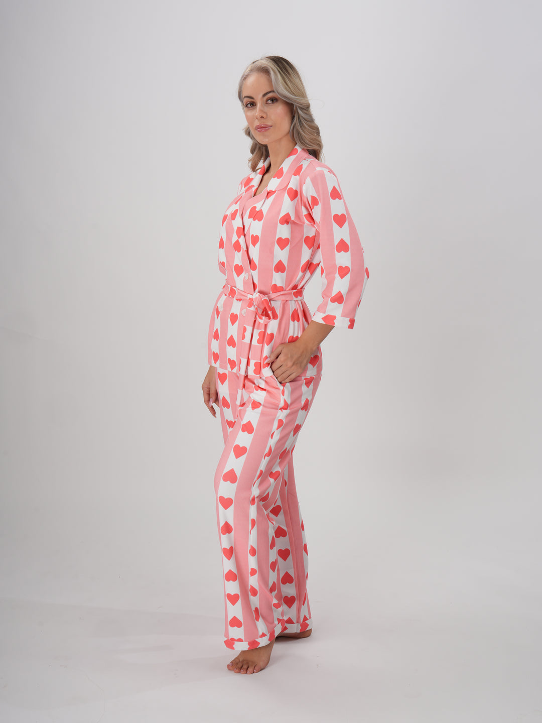 A model wearing a pink hearts pajama set with a collar and full sleeves. The set includes a detachable belt.