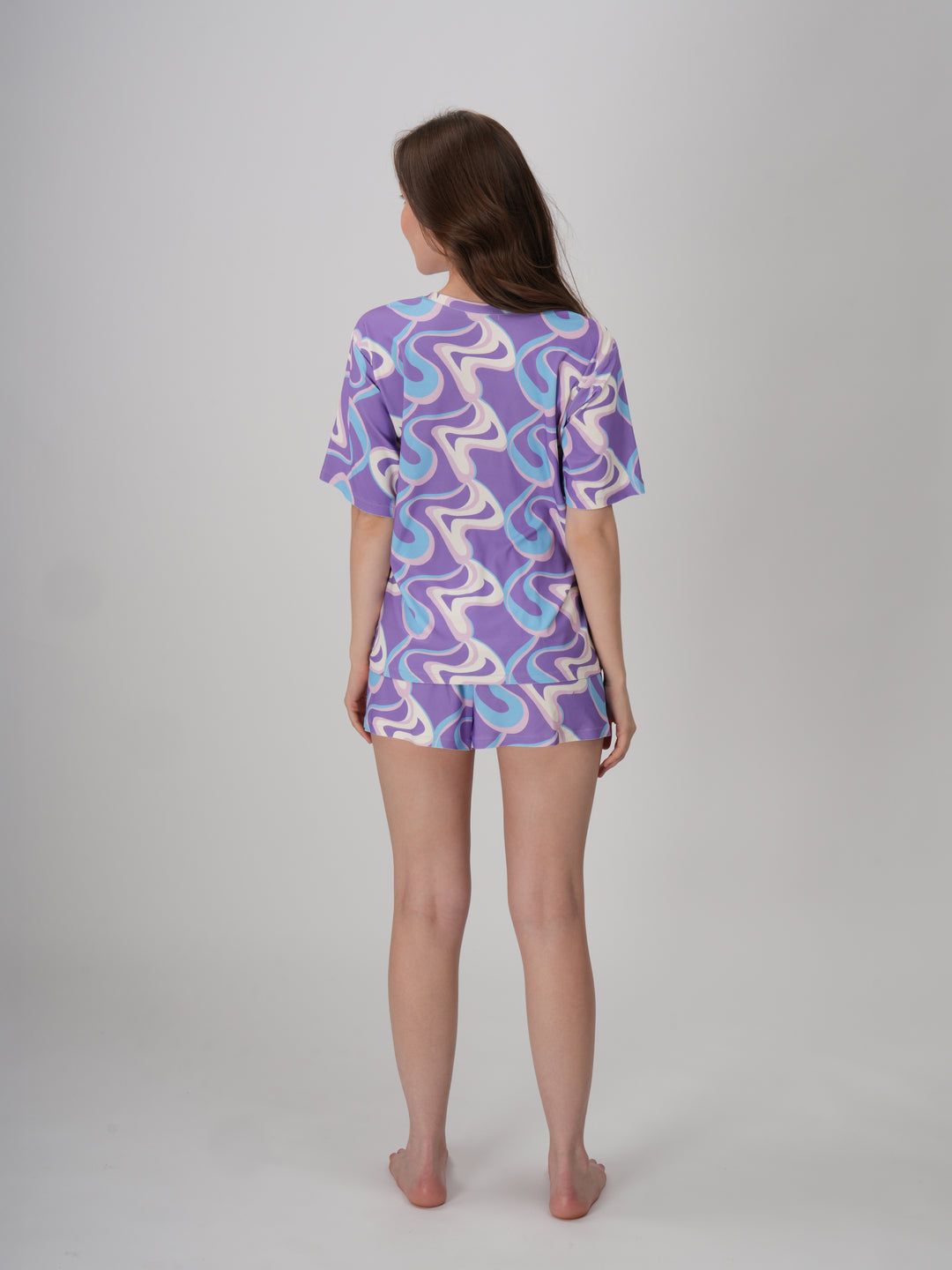 A model wearing a lavender and blue geometric patterned short set with a slim fit top and mid-rise pajama shorts - Lavender Twirls Short Set.