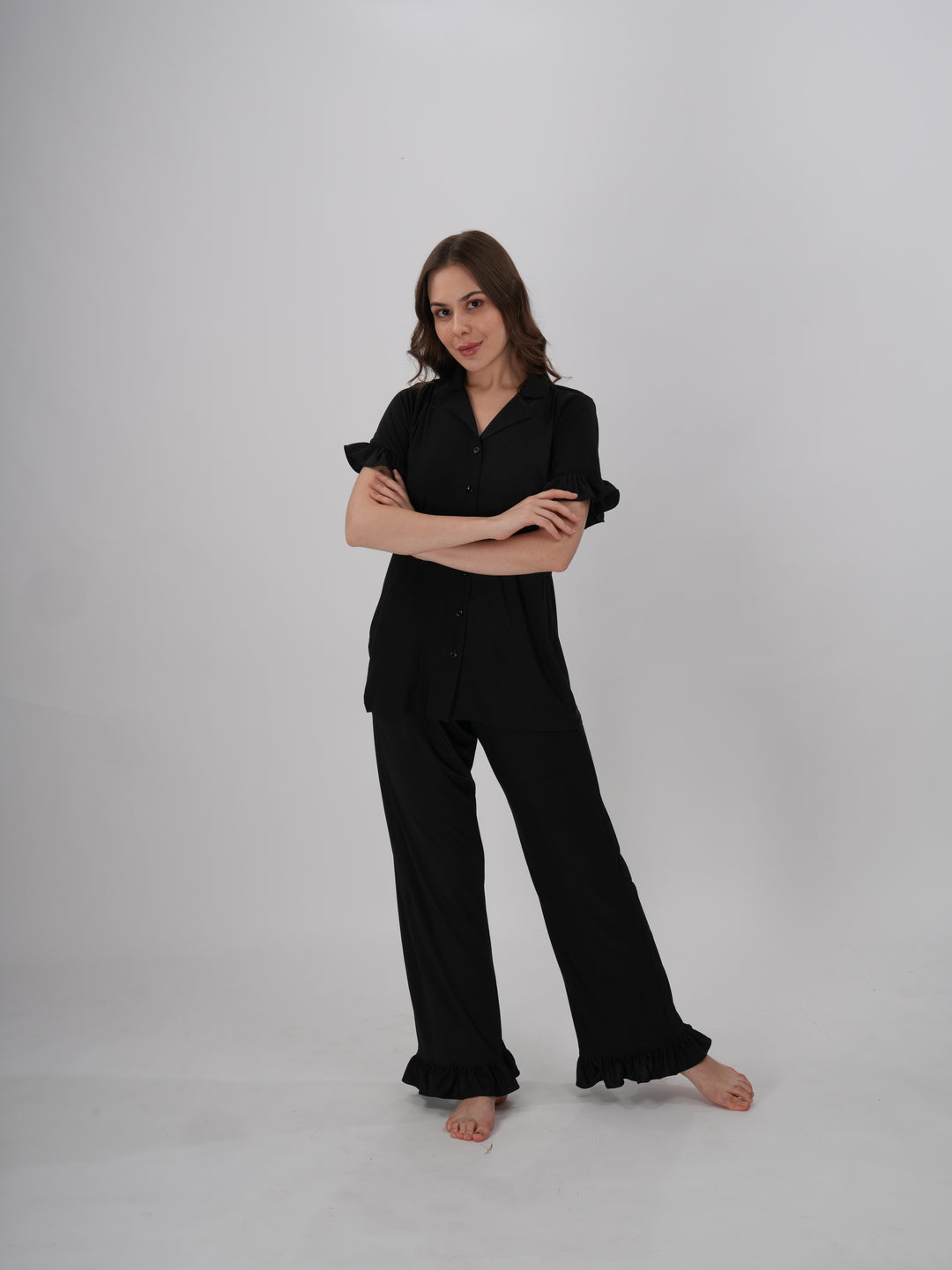 A woman wearing a black two-piece lounge set with ruffled details on the sleeves and pants - Midnight Ruffle PJ Set