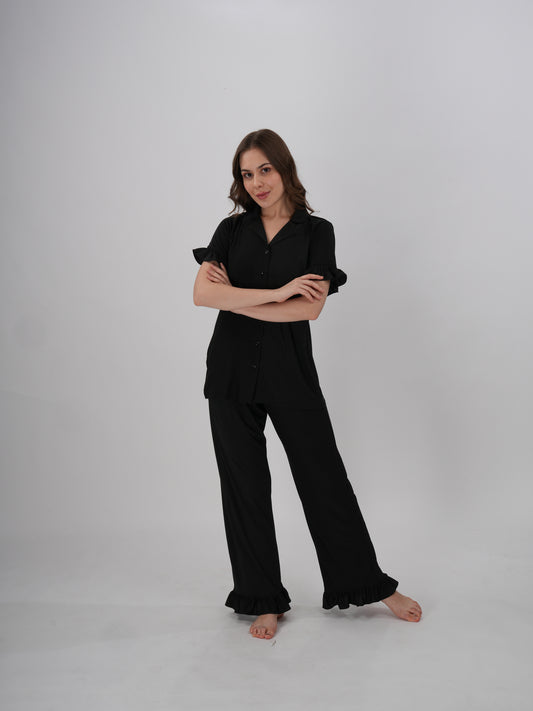 A woman wearing a black two-piece lounge set with ruffled details on the sleeves and pants - Midnight Ruffle PJ Set