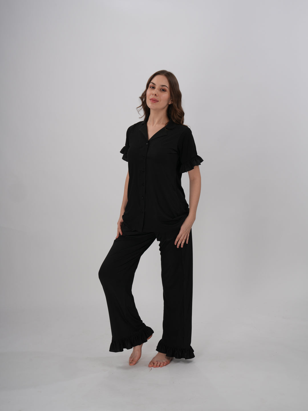 A woman wearing a black two-piece lounge set with ruffled details on the sleeves and pants - Midnight Ruffle PJ Set