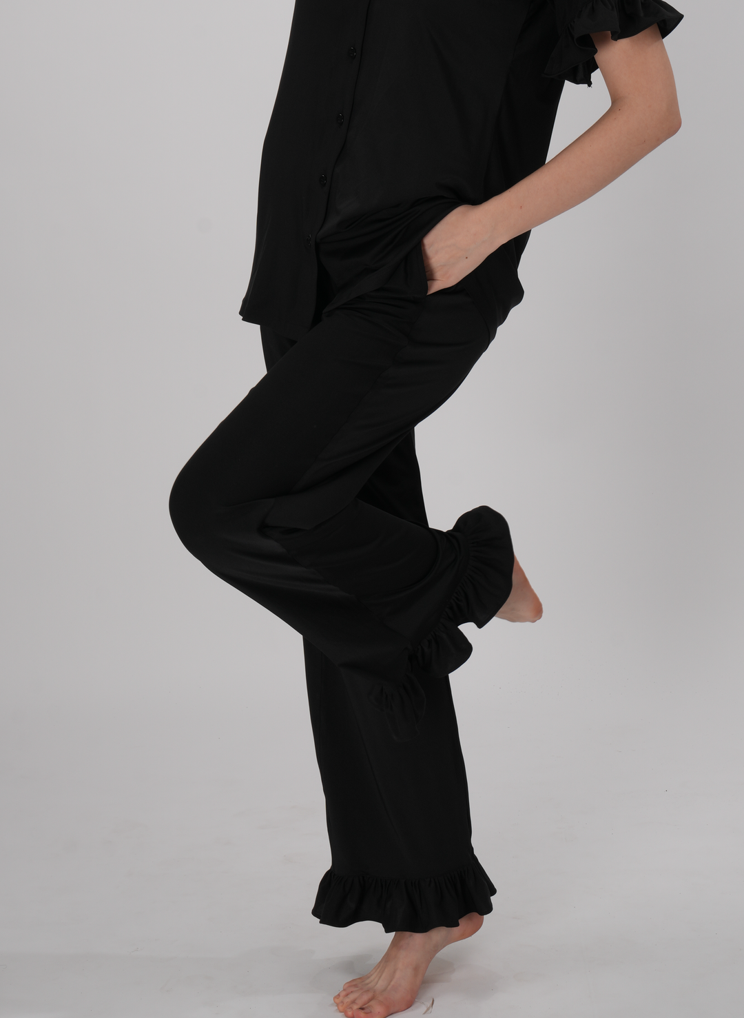 A woman wearing a black two-piece lounge set with ruffled details on the sleeves and pants - Midnight Ruffle PJ Set