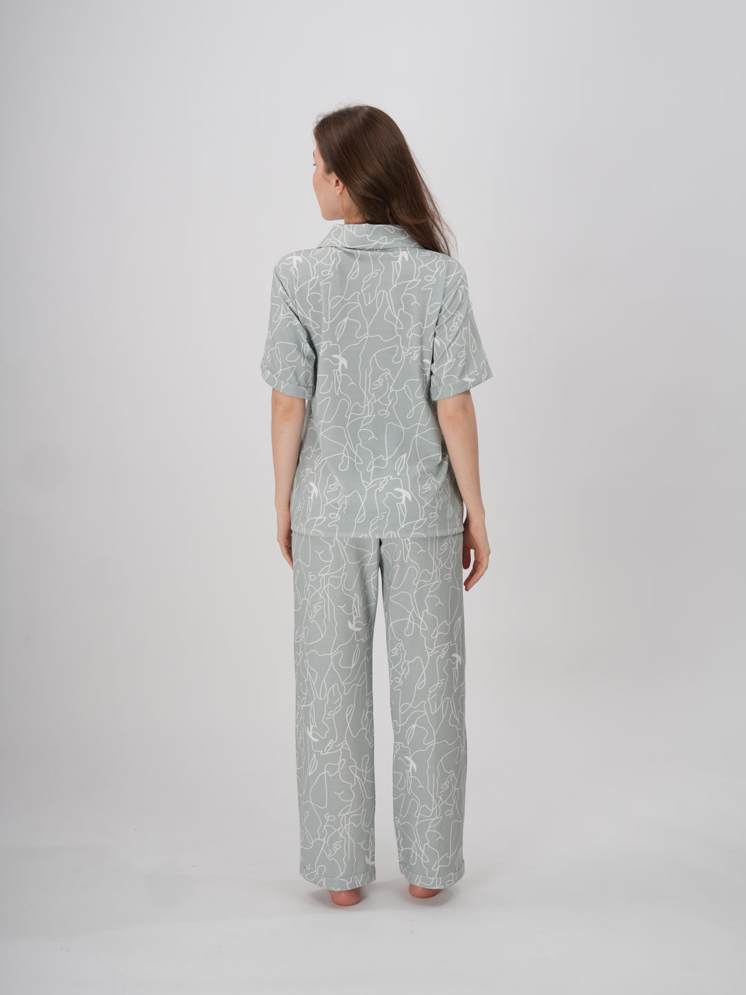 A woman standing, wearing a short-sleeved, full-length pajama set with an abstract line print - Serene Lines PJ Set