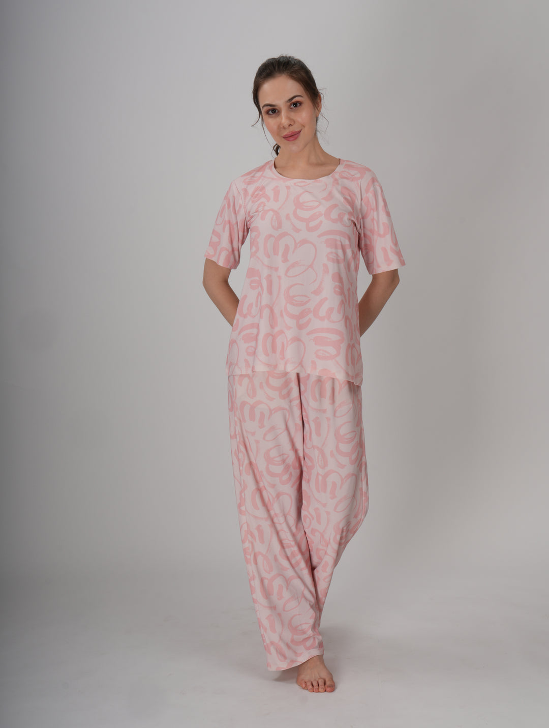 A woman standing, wearing a short pink PJ set with a round neckline and elastic waistband - Soft Pink Seam PJ Set.