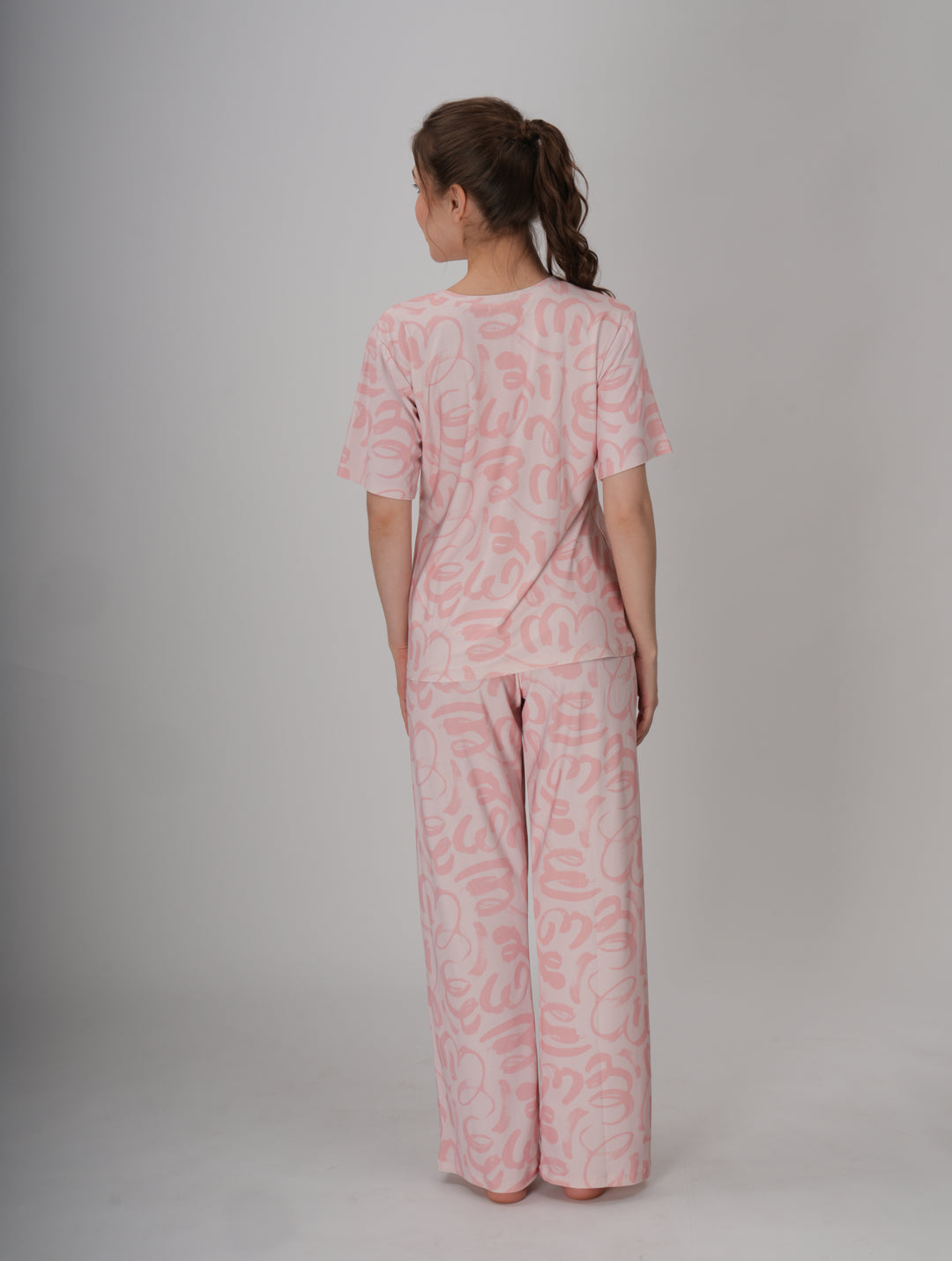 A woman standing, wearing a short pink PJ set with a round neckline and elastic waistband - Soft Pink Seam PJ Set.