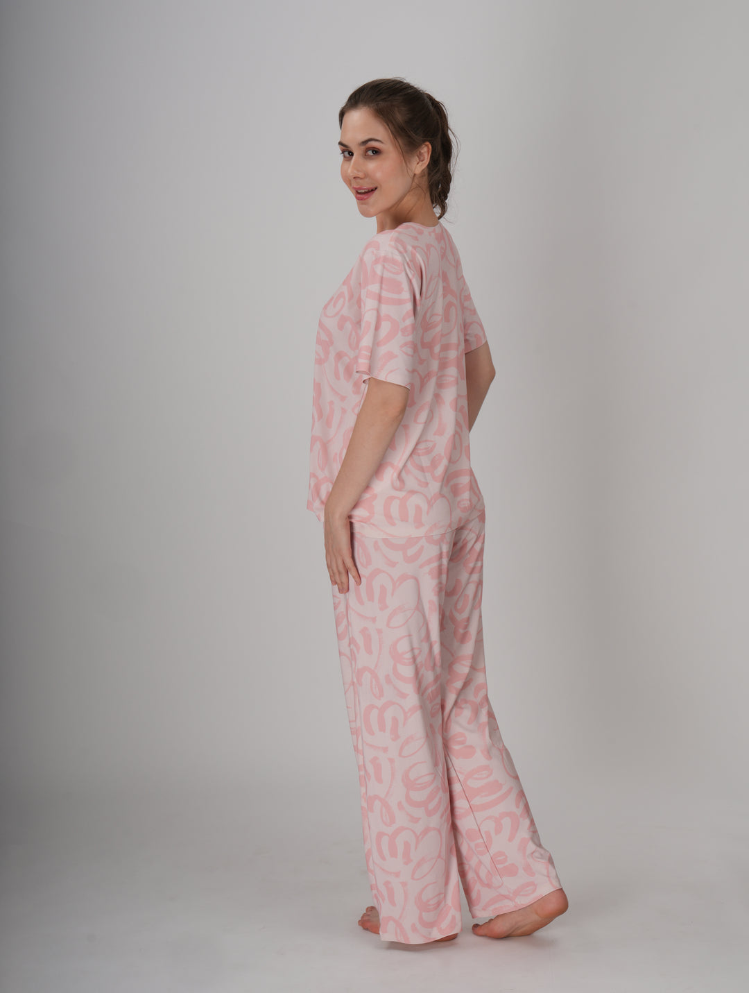 A woman standing, wearing a short pink PJ set with a round neckline and elastic waistband - Soft Pink Seam PJ Set.