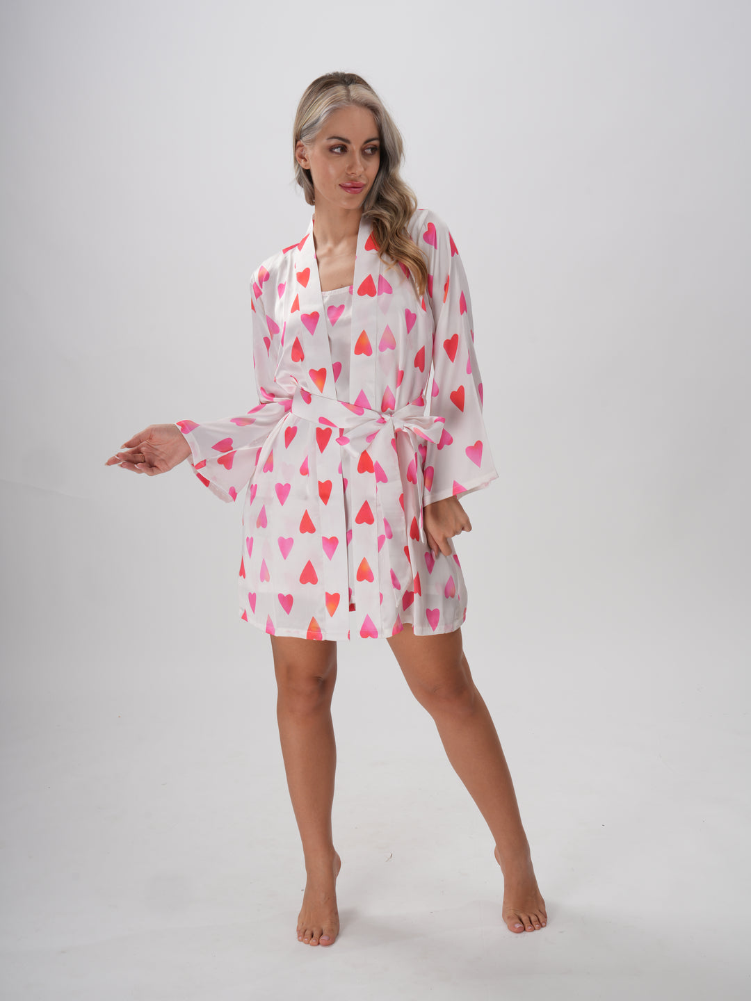Woman wearing a pink and white robe with all-over heart print, V-neckline, and adjustable waist tie – Sweetheart Robe