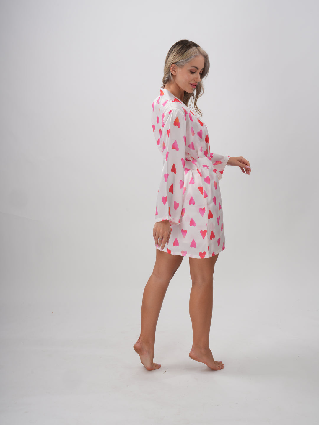 Woman wearing a pink and white robe with all-over heart print, V-neckline, and adjustable waist tie – Sweetheart Robe
