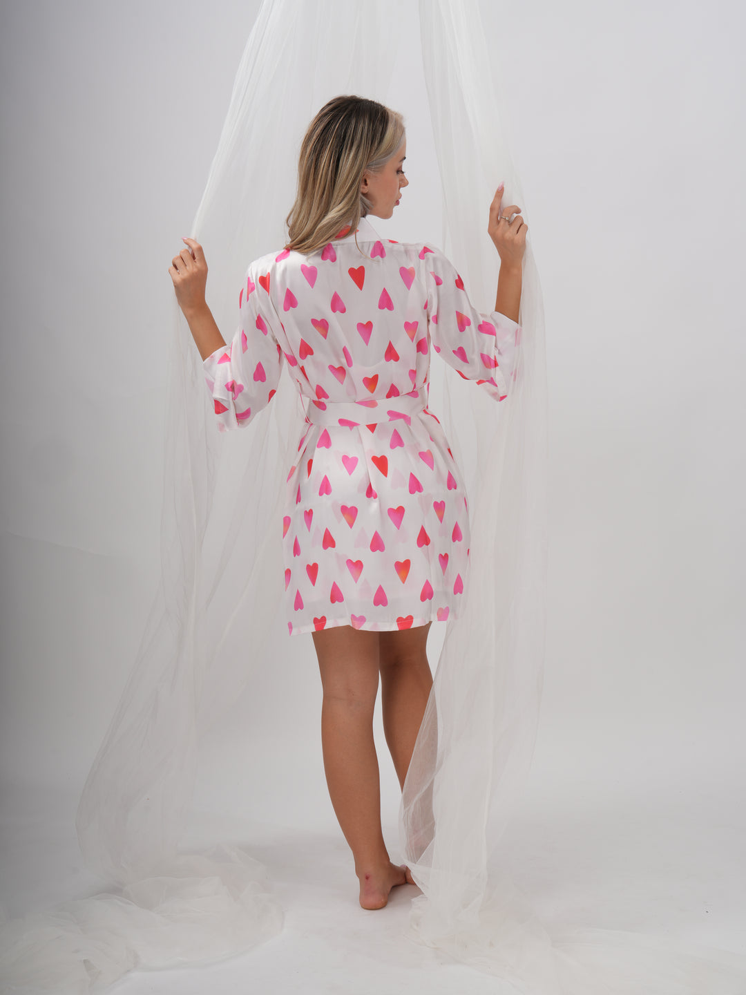 Woman wearing a pink and white robe with all-over heart print, V-neckline, and adjustable waist tie – Sweetheart Robe